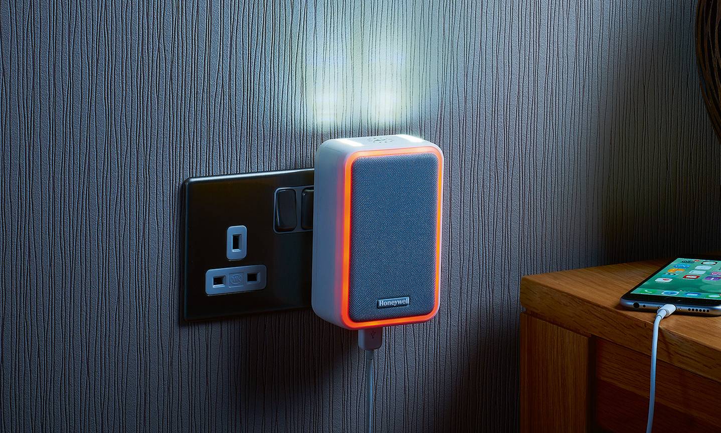 Door bell with illuminated rim plugged into a wall, a side table with a vase, a phone and keys