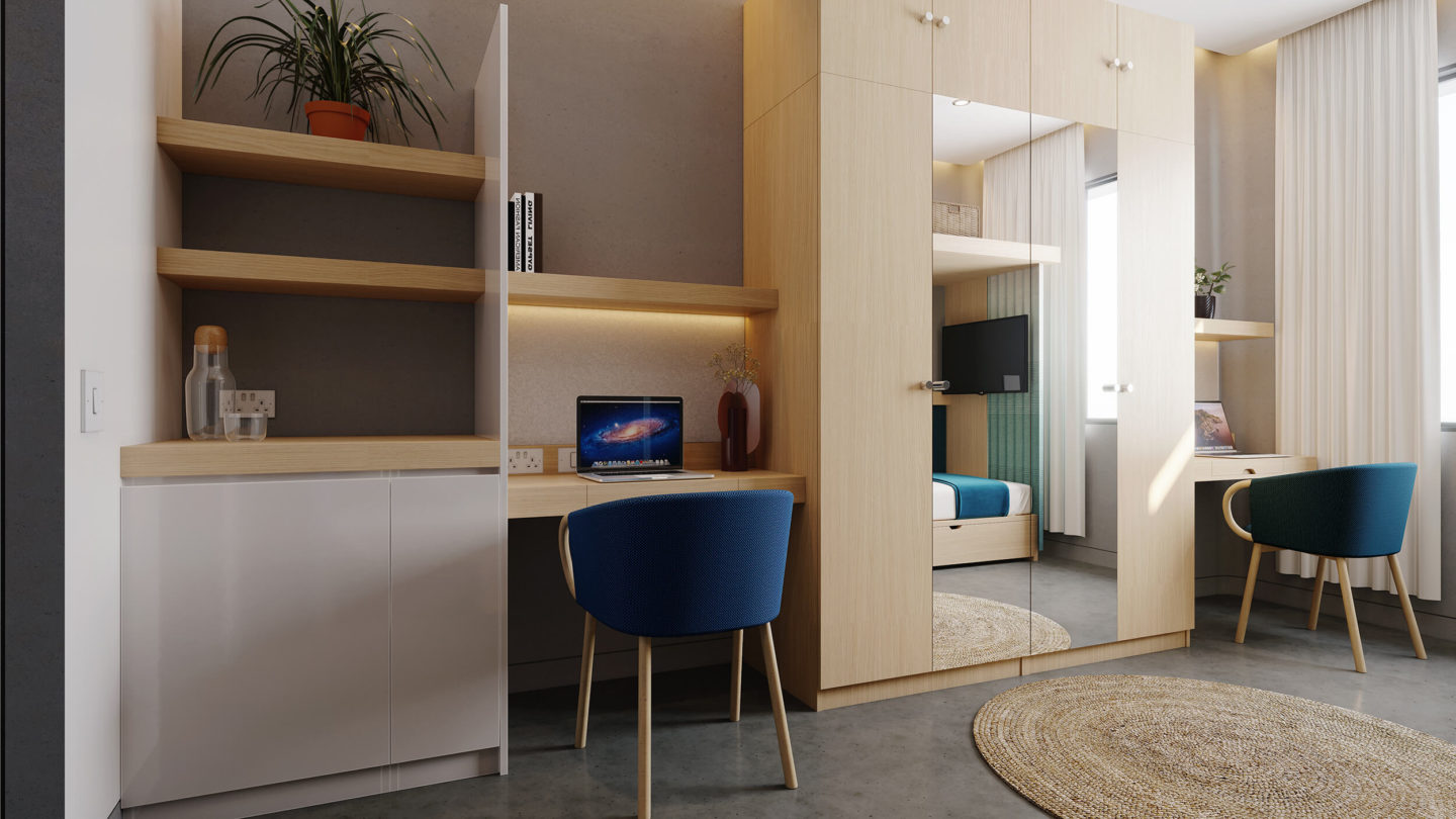 A room interior with a large wardrobe with two mirrored doors. Two desks and chairs can be seen on either side. There is a shelf above each desk. On the far left is a storage unit with two shelves above