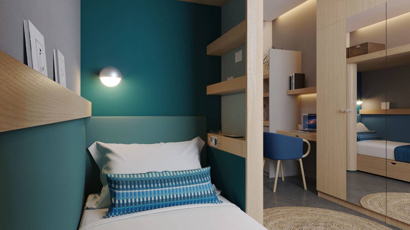 Close up view of a bed taken from the foot of the bed. A desk, chair and wardrobe with mirrored doors is seen across the room