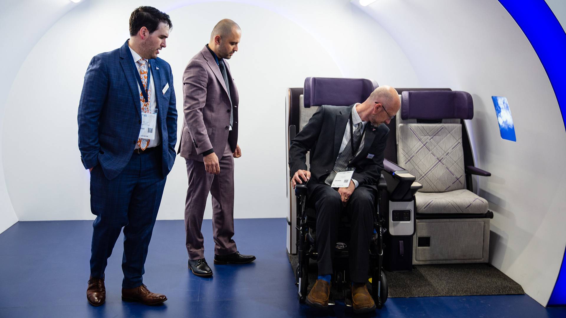 Air for All protoype at AIX 2023 being tested. One person in a powered wheelchair backing into the seat, two people watching the demonstration.
